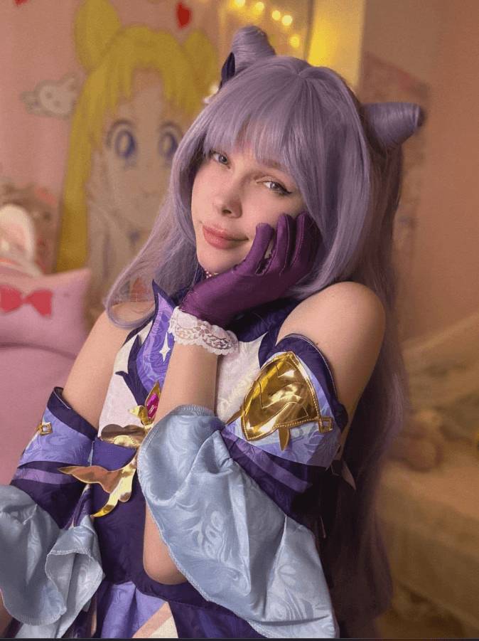 Cosplayer with lavender wig and cat-ear headband, wearing a purple-blue fantasy costume, resting her chin on gloved hand in a soft pose.
