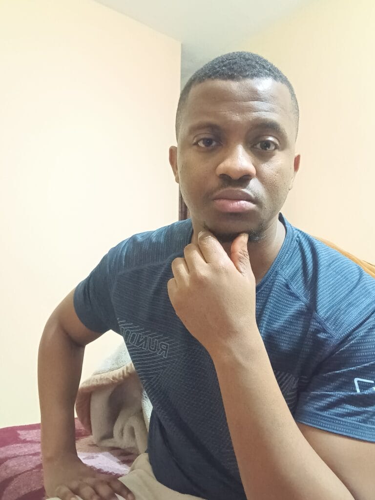 Close-up of a young man thinking, hand on chin, wearing a blue athletic shirt indoors.