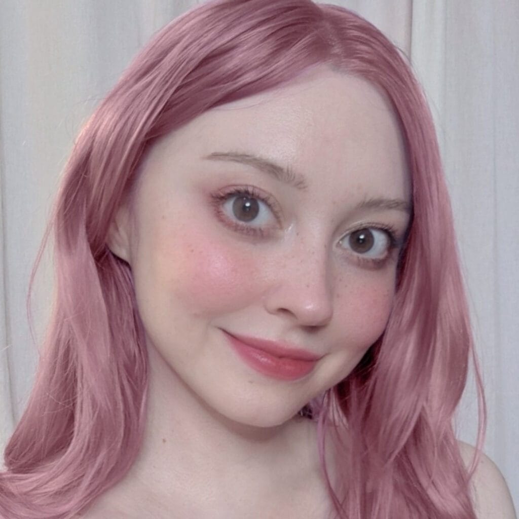 Close-up of a woman with pink hair, brown eyes, and a gentle smile, looking to the side
